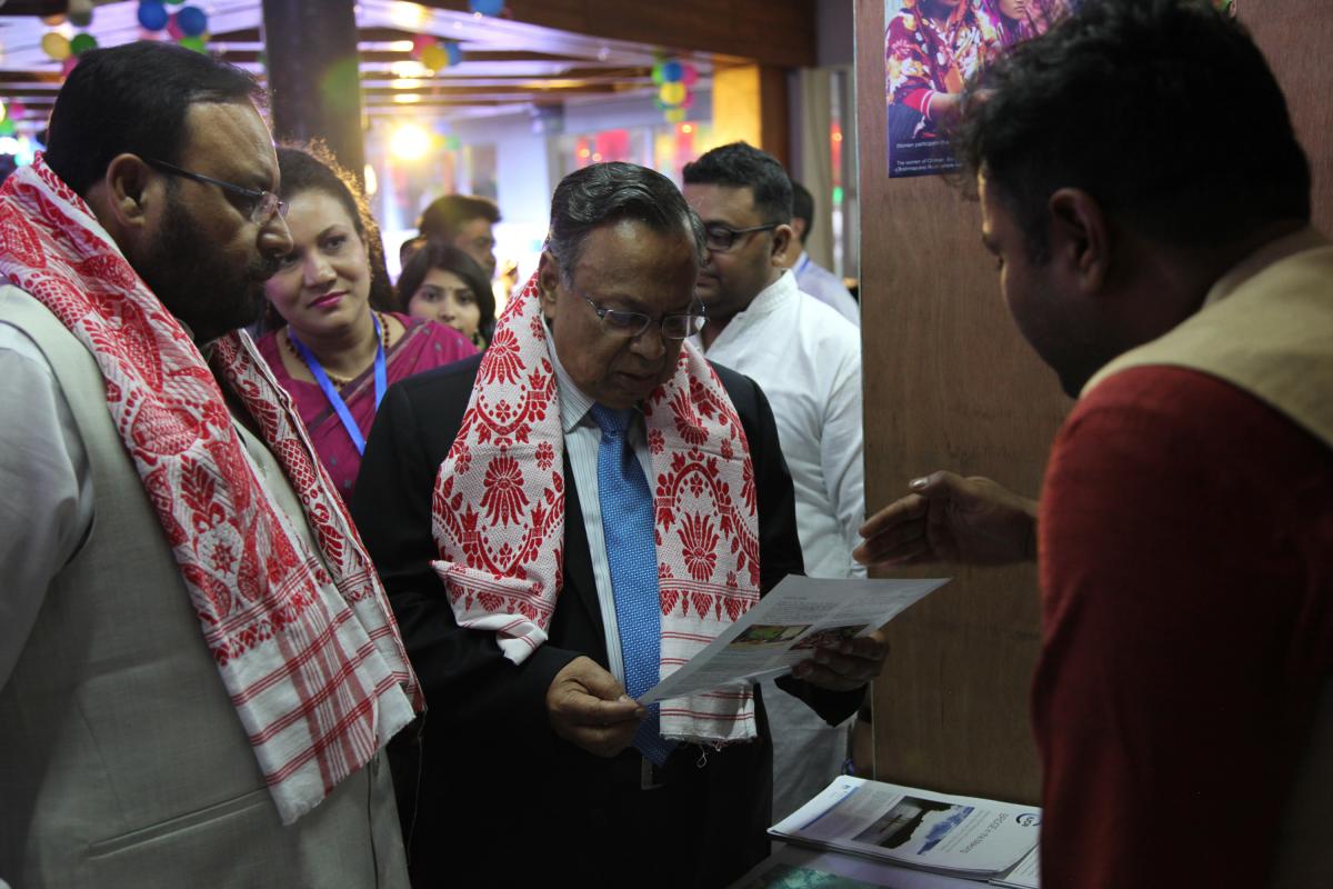 Two men wearing red patterned scarves read a flyer at the BRIDGE GBM booth