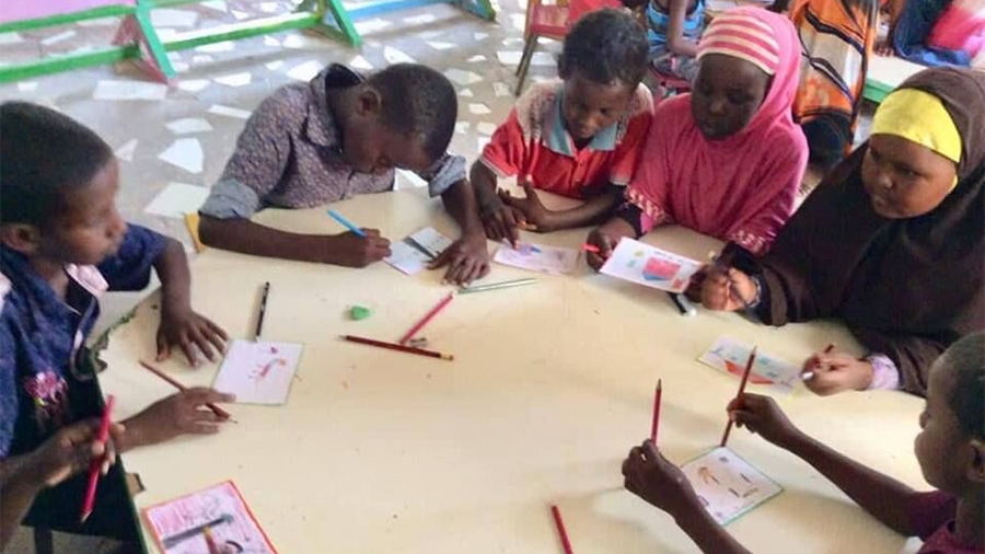 Children in Somalia gathered around a table drawing their postcards message