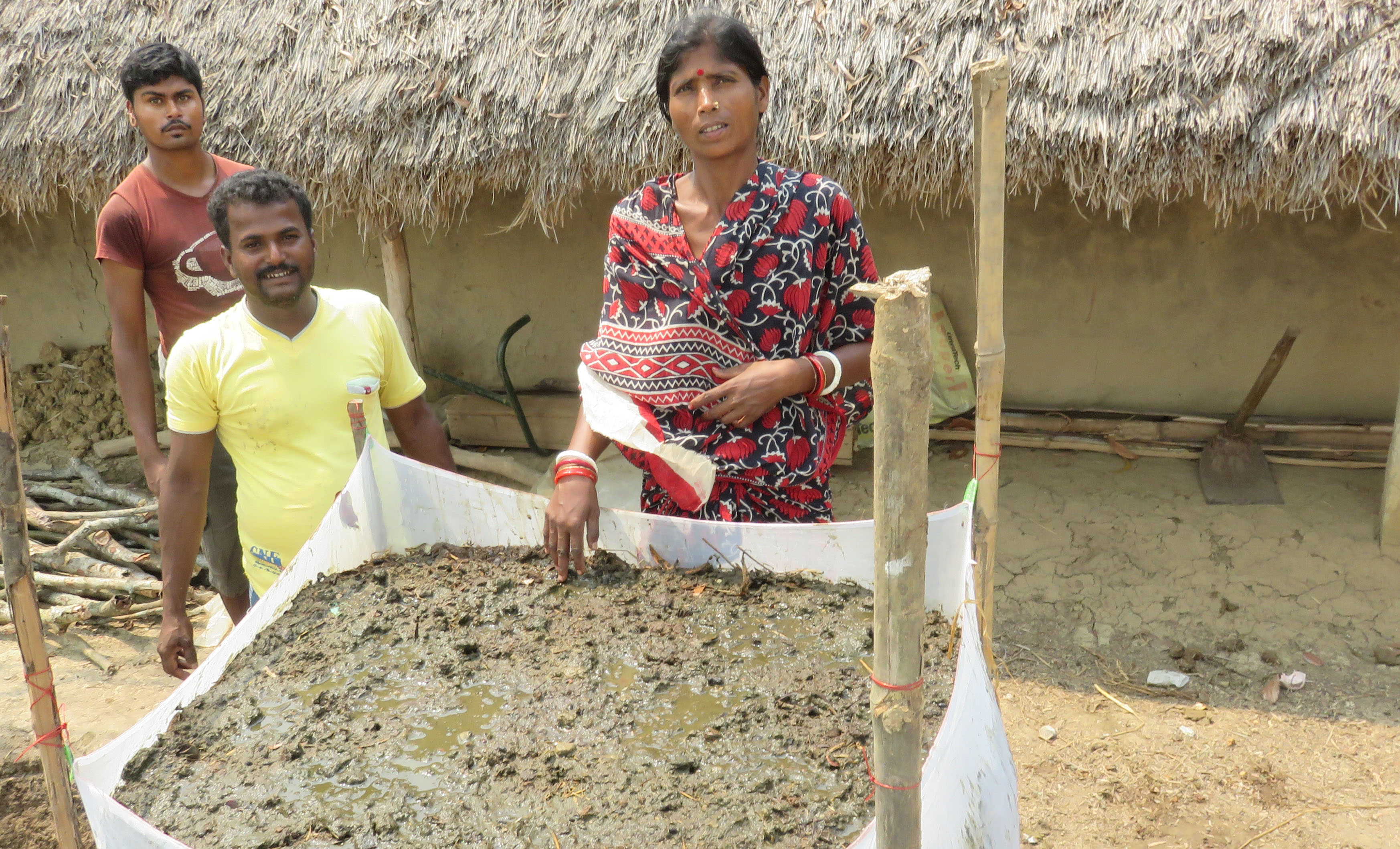 A woman stands next to a large basin full of vermicompost, with two men beside her