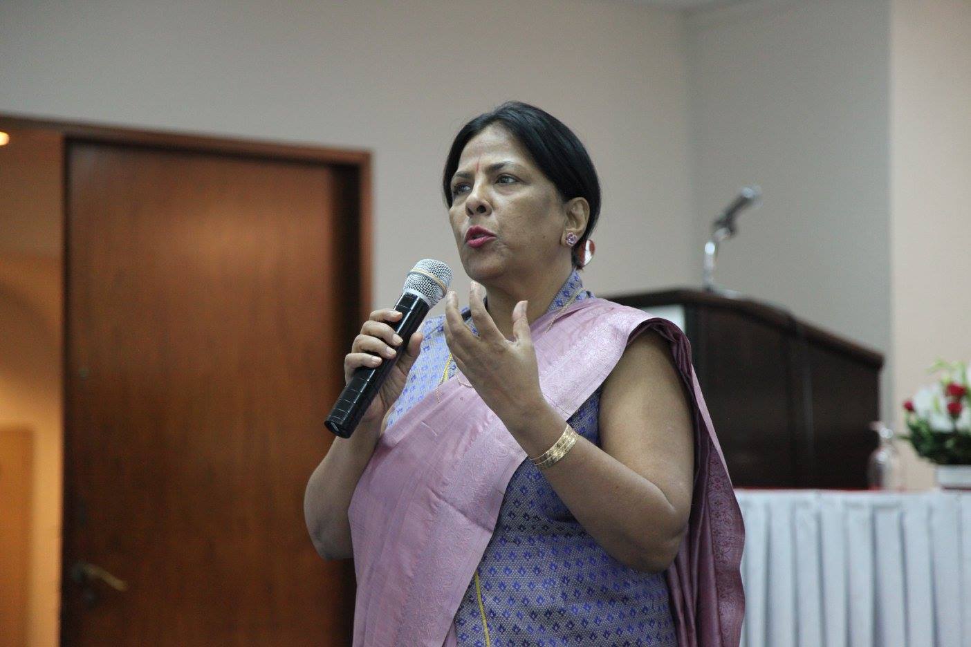A woman in a purple sari speaks into a microphone