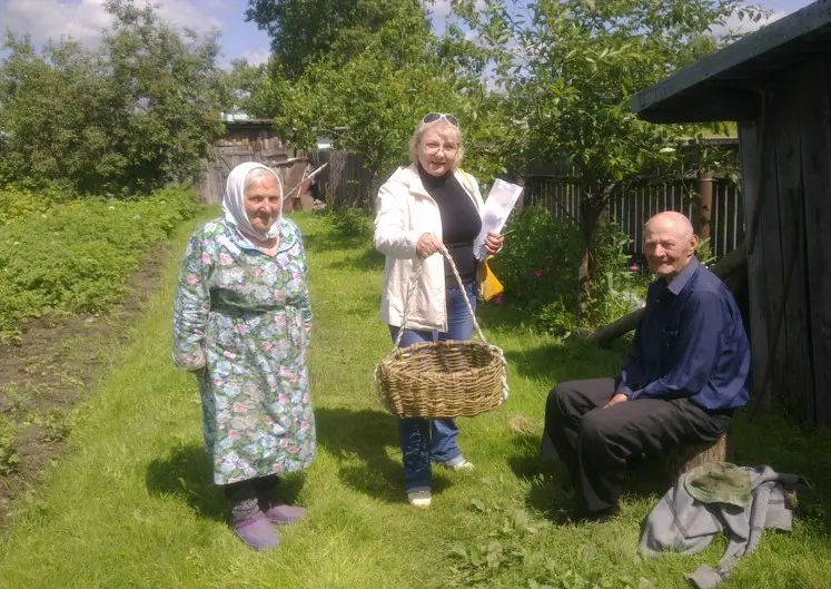 Two elderly people and another woman with a clipboard and basket in a garden