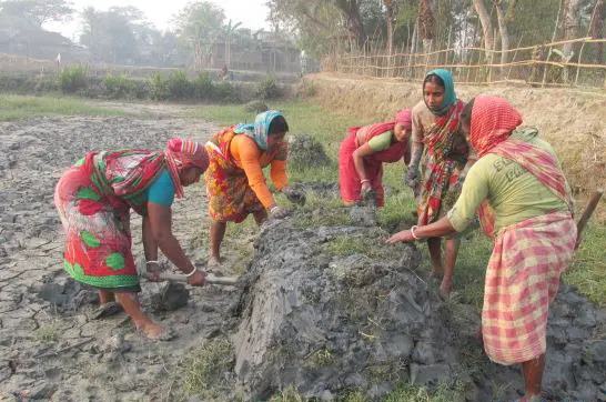 Five women dressed in bright colors construct a waist-high wall out of mud